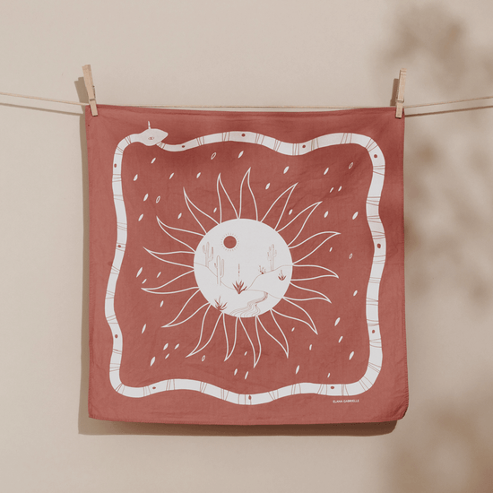 Terracotta bandana with printed illustration of a white snake, sun, and desert scene.