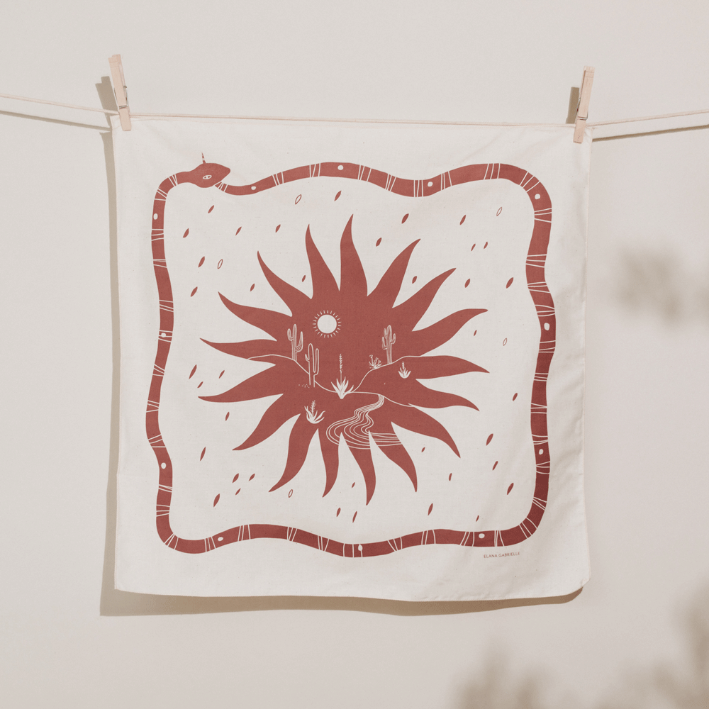 Natural undyed bandana with printed illustration of a terracotta snake, sun, and desert scene.