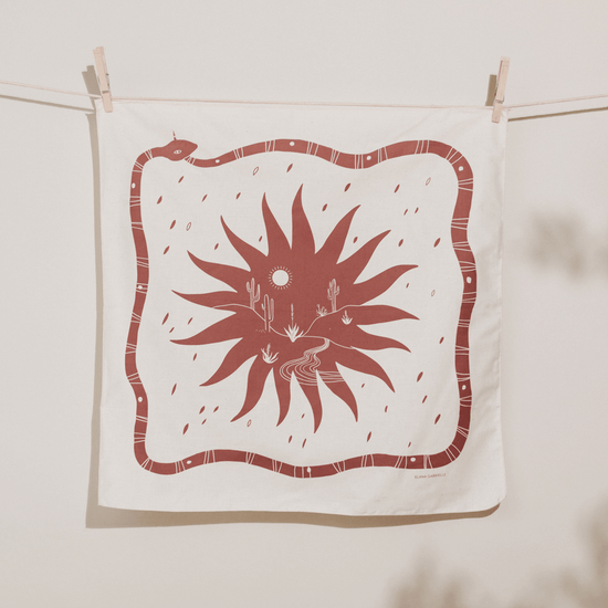 Natural undyed bandana with printed illustration of a terracotta snake, sun, and desert scene.